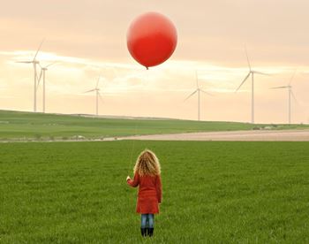 Mädchen mit rotem Luftballon steht vor Windrädern als Symbol für nachhaltige Geldanlagen