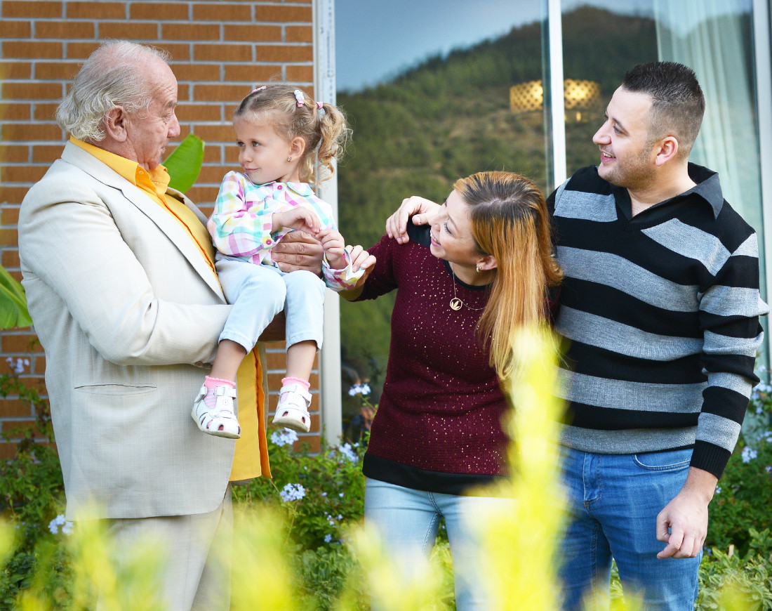 Familie steht im Garten vor dem Haus, Opa trägt Enkelin auf dem Arm