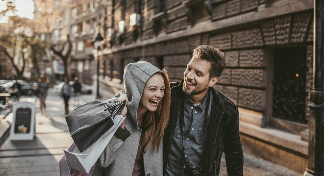 Pärchen kommt vom Shopping, sie trägt Einkaufstaschen über der Schulter