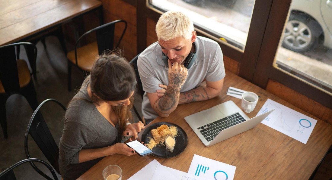Zwei junge Leute sitzen im Café und bezahlen mit Bitcoin per Smartphone