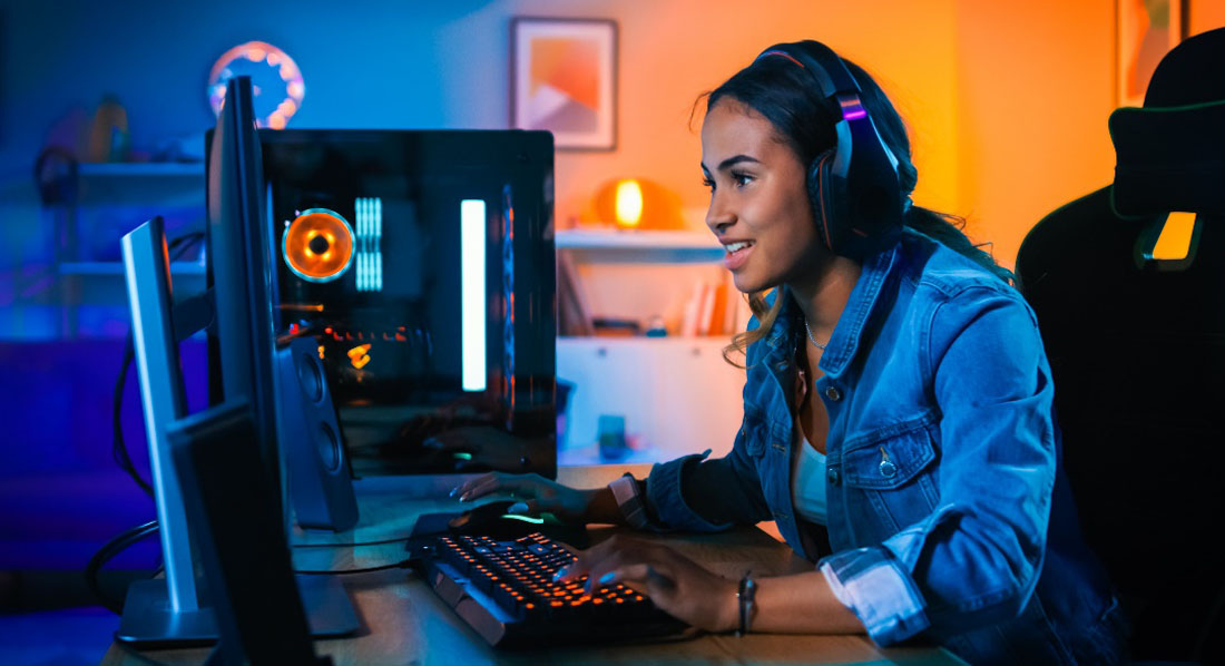 Junge Frau mit Kopfhörern sitzt spielend vor einem Computerbildschirm