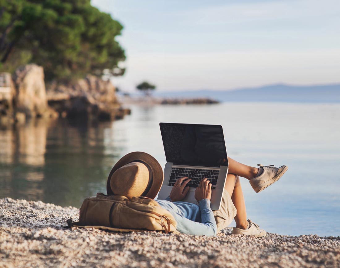 Junge Frau liegt mit Laptop am Strand