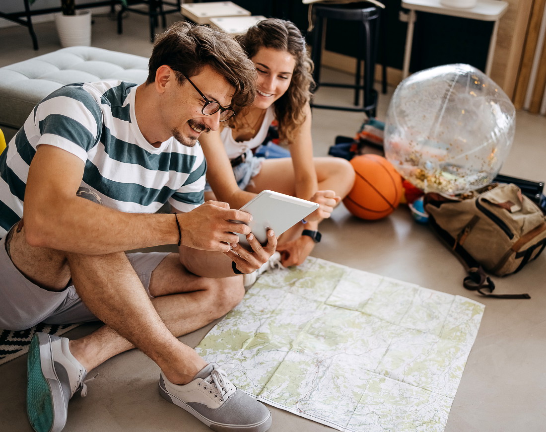 Ein junges Pärchen sitzt vor einer Mappe auf dem Boden und schaut auf ein iPad