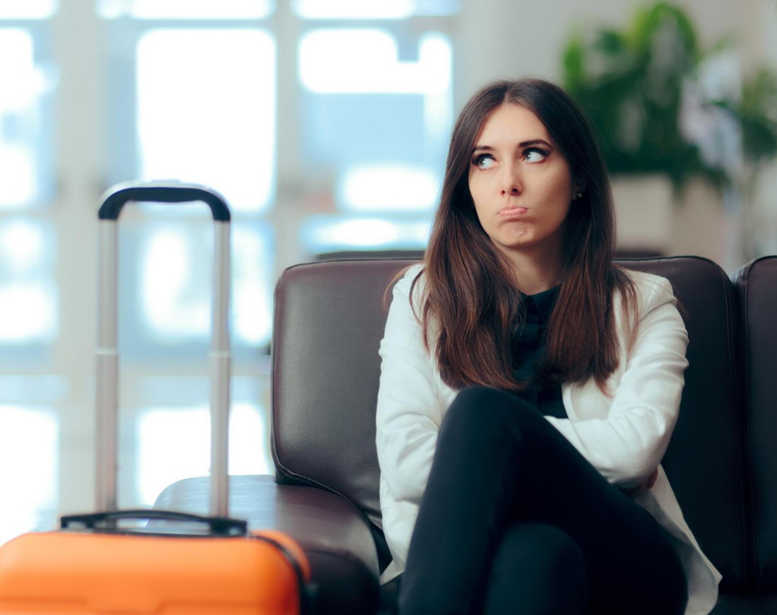 Eine junge Frau sitzt nachdenklich neben ihrem Trolley in einer Flughafen-Wartehalle