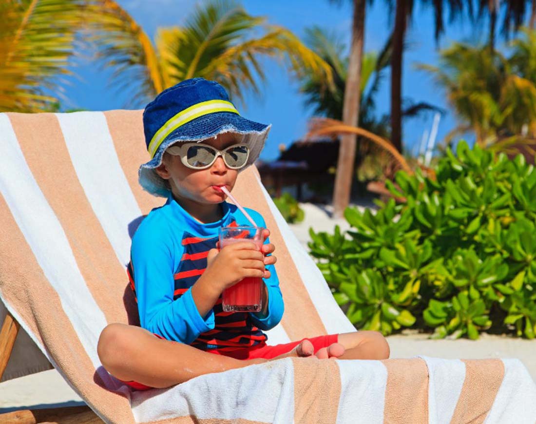 Junge mit Sonnenbrille und Cocktail auf einer Liege in tropischer Kulisse