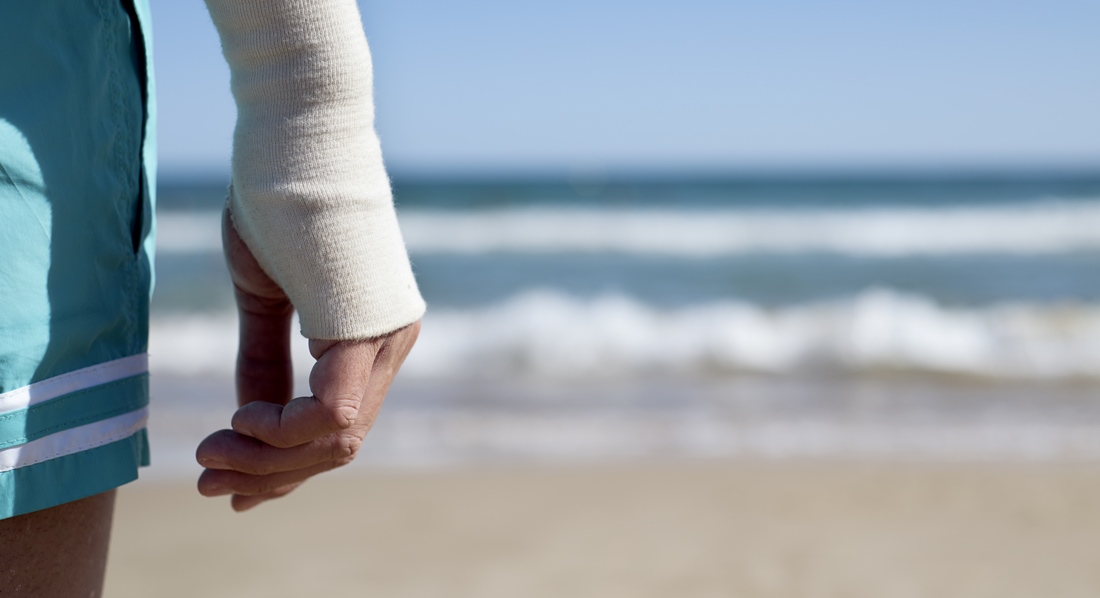 Mann in Shorts mit Verband am rechten Handgelenk am Strand