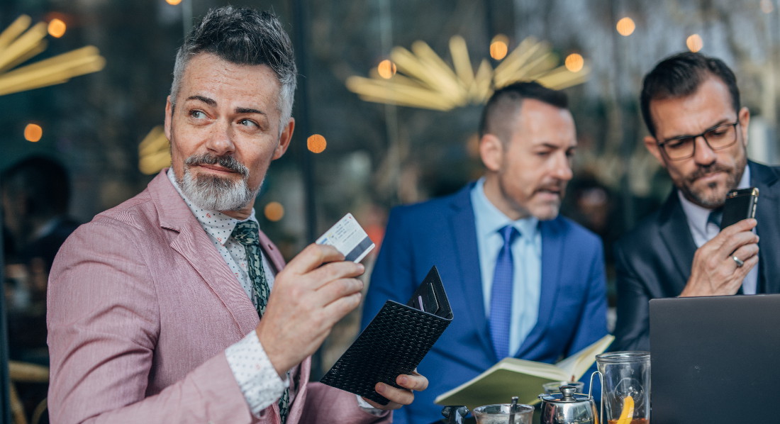 Ein Geschäftsmann zahlt im Restaurant mit Kreditkarte, im Hintergrund sind zwei weitere Männer ins Gespräch vertieft