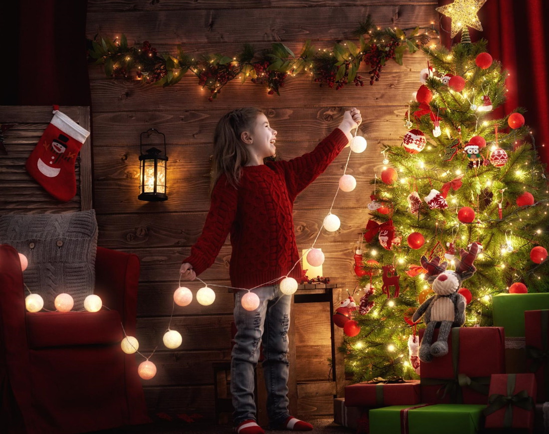 Kind bringt Lichterkette am Weihnachtsbaum an