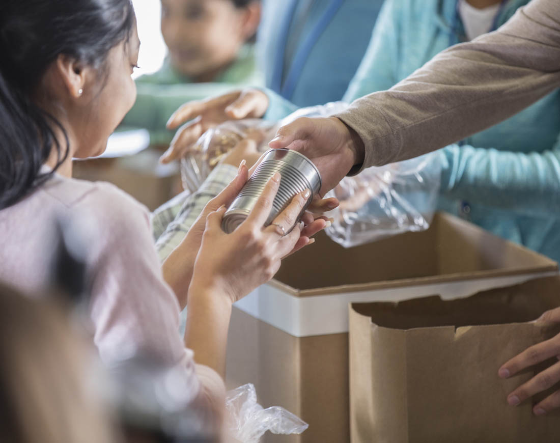 Helfer verteilen aus einem Karton Lebensmittelkonserven an bedürftige Kinder