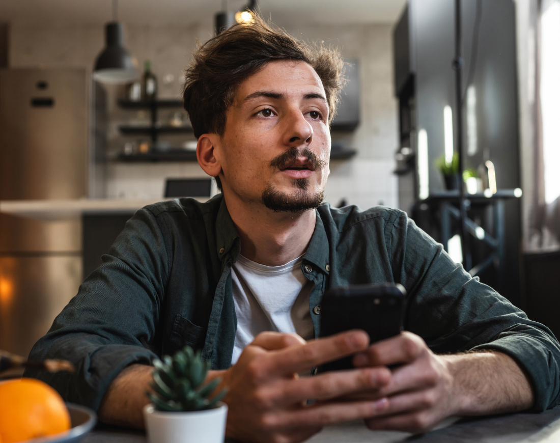 Ein skeptisch blickender Mann hält ein Handy, während er an einem Tisch sitzt