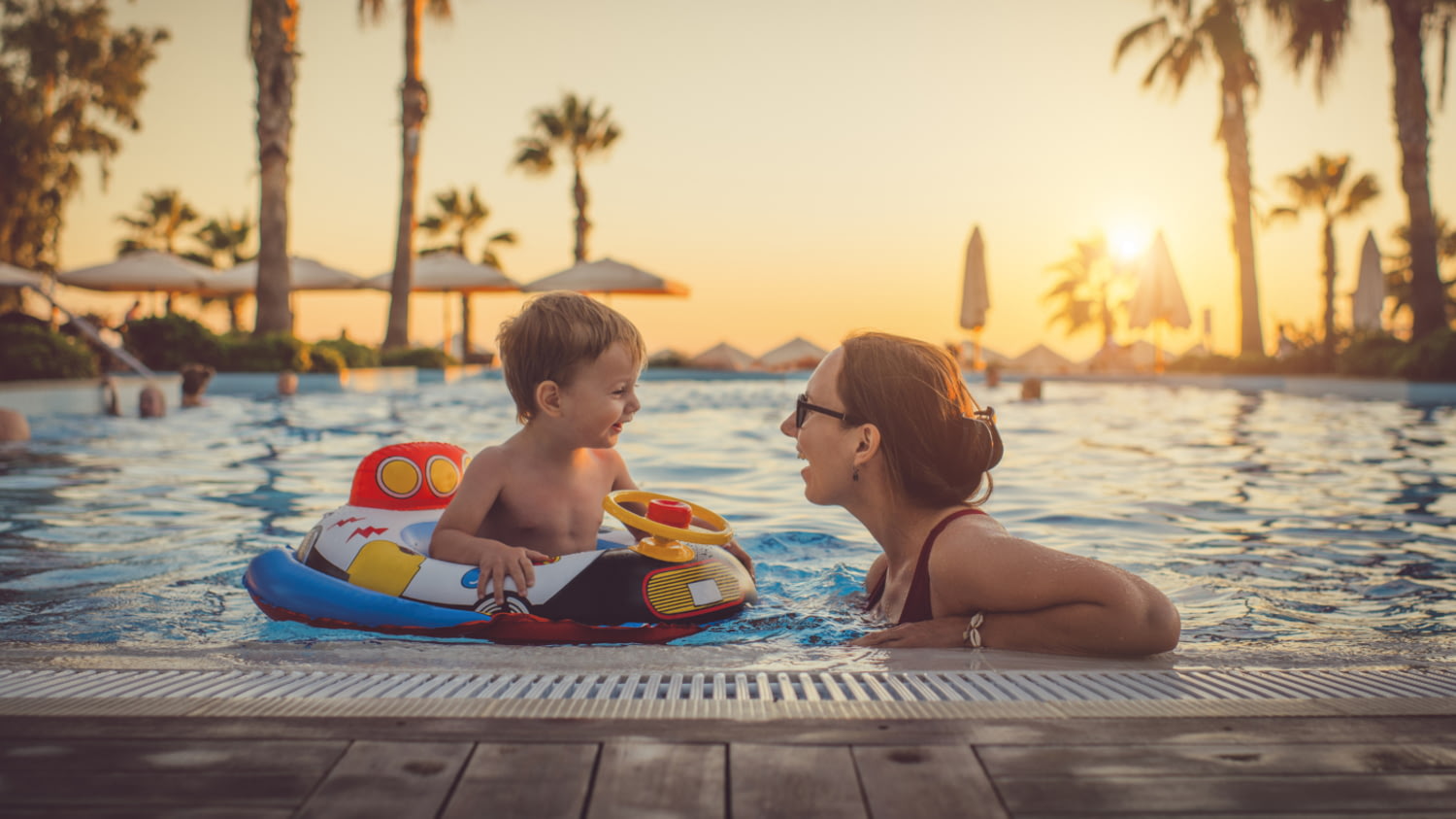 Eine Mutter mit ihrem Kind im Schwimmbad vor einem tropischen Hintergrund