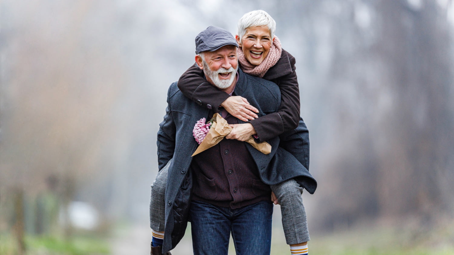 Älterer Mann trägt ältere Frau huckepack im Park