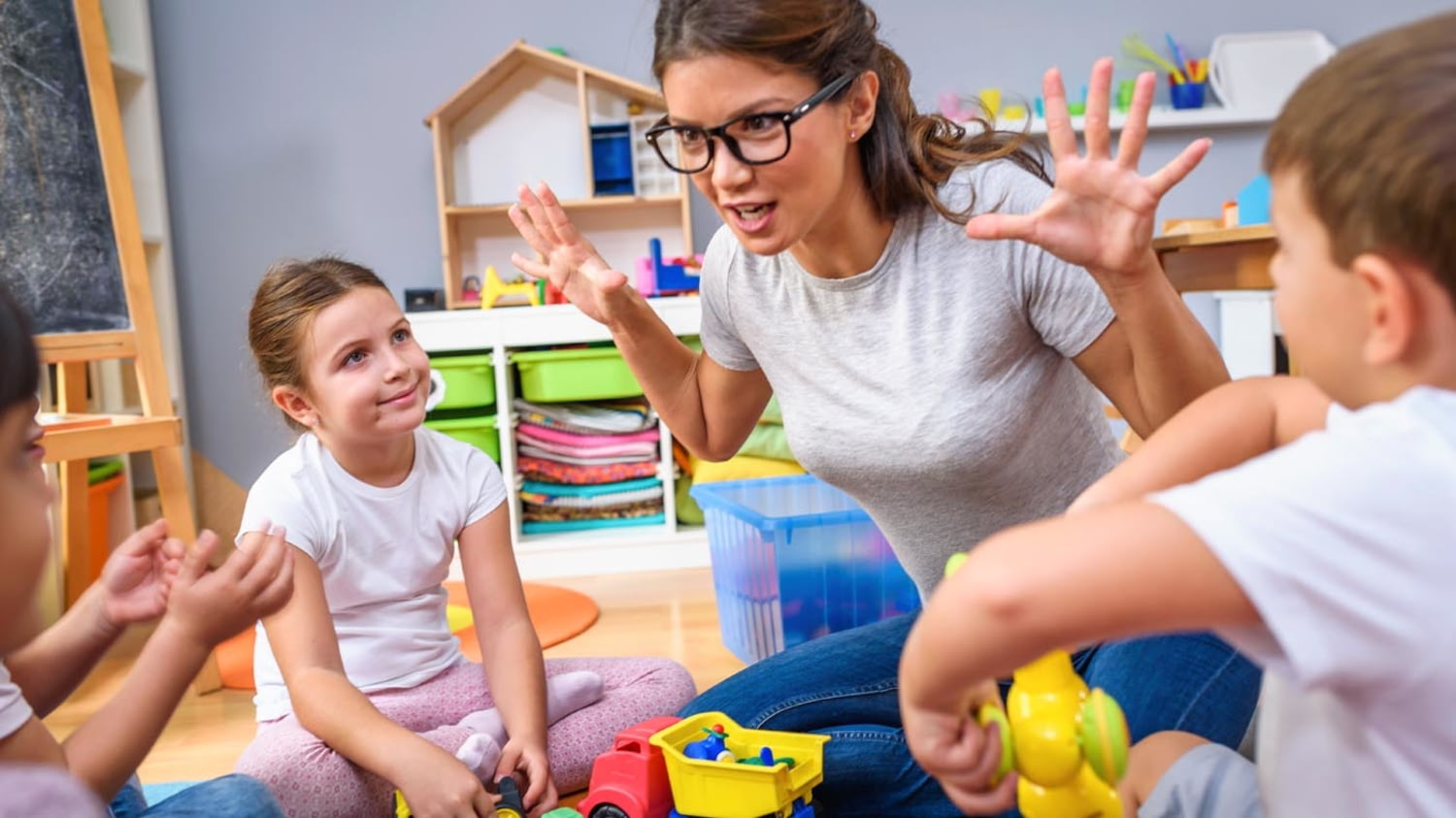 Junge Erzieherin erzählt einer Gruppe von Kindergartenkindern gestenreich eine Geschichte