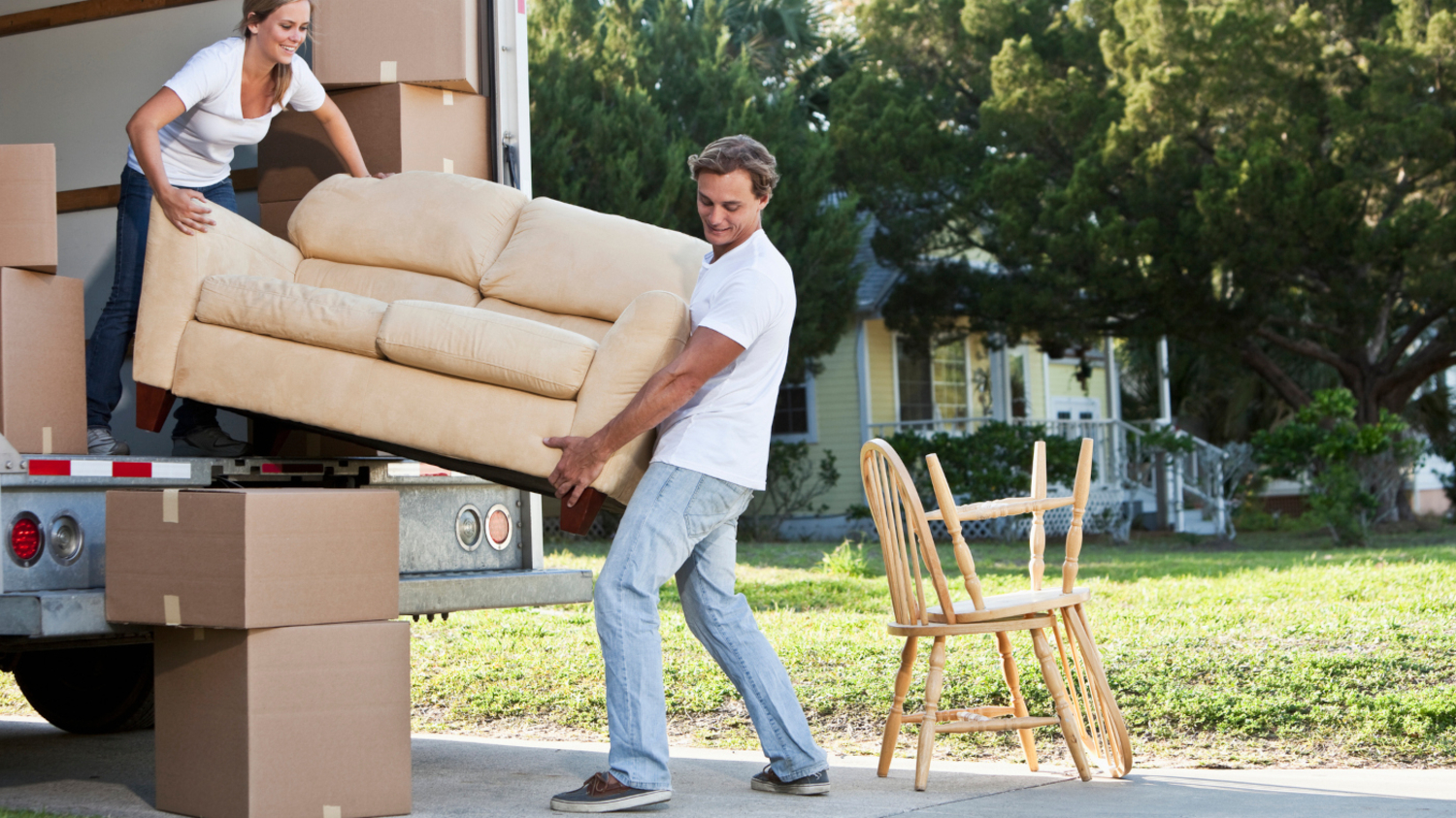 Junges Pärchen lädt helles Sofa aus einem Umzugswagen
