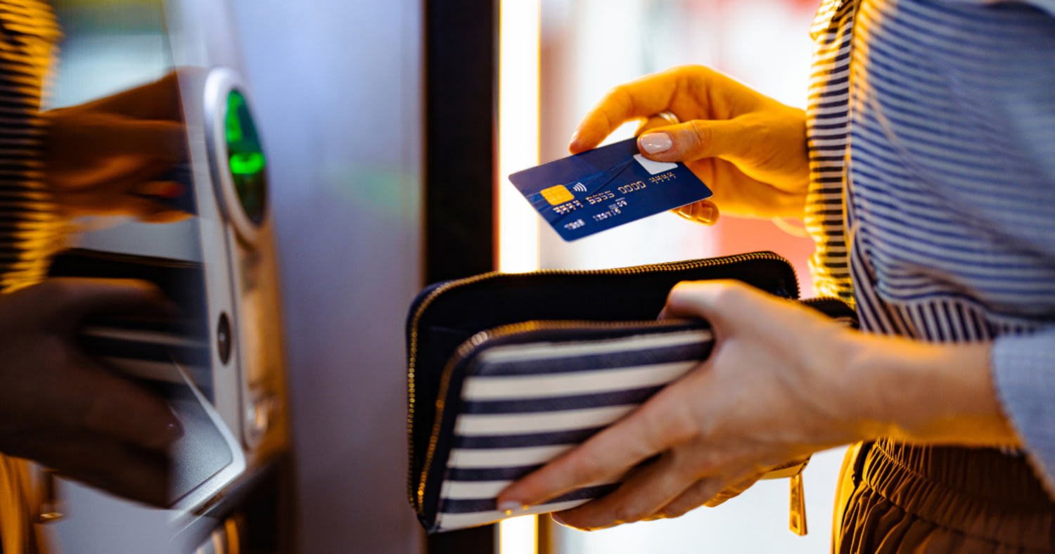 Nahaufnahme von Frauenhänden mit einer Debitkarte vor einem Geldautomaten