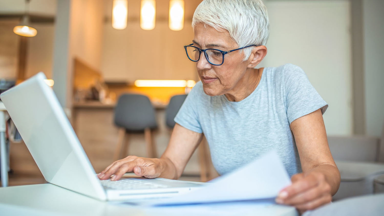 Frau gleicht Informationen auf einem Blatt Papier mit Daten auf ihrem Computer ab.