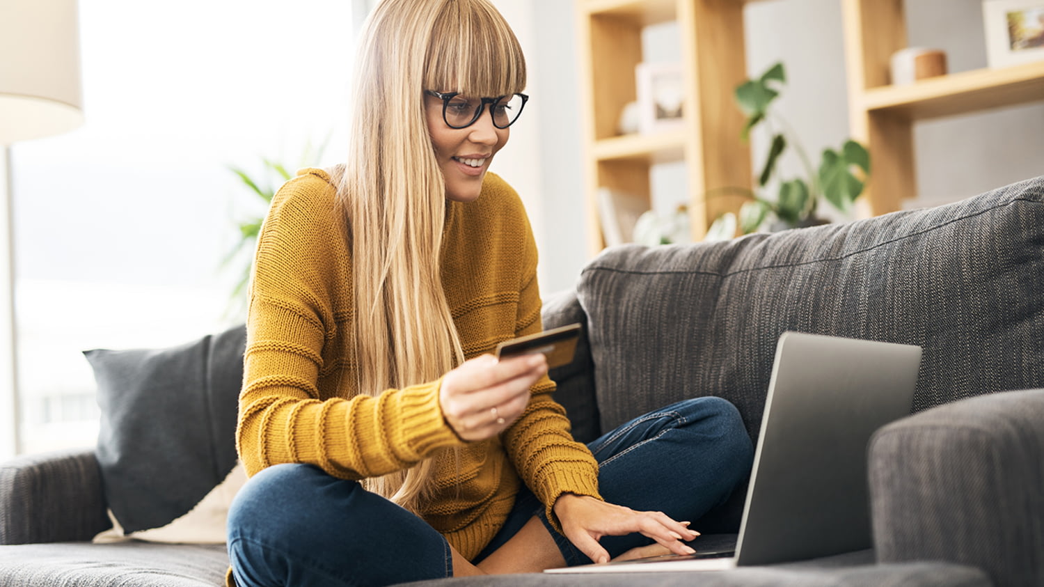Eine Frau sitzt auf dem Sofa, mit Laptop neben ihr und Kreditkarte in der Hand