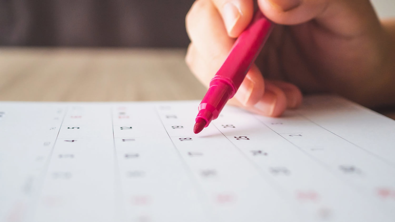 Eine Hand führt einen roten Stift, um einen Eintrag im Kalender zu machen