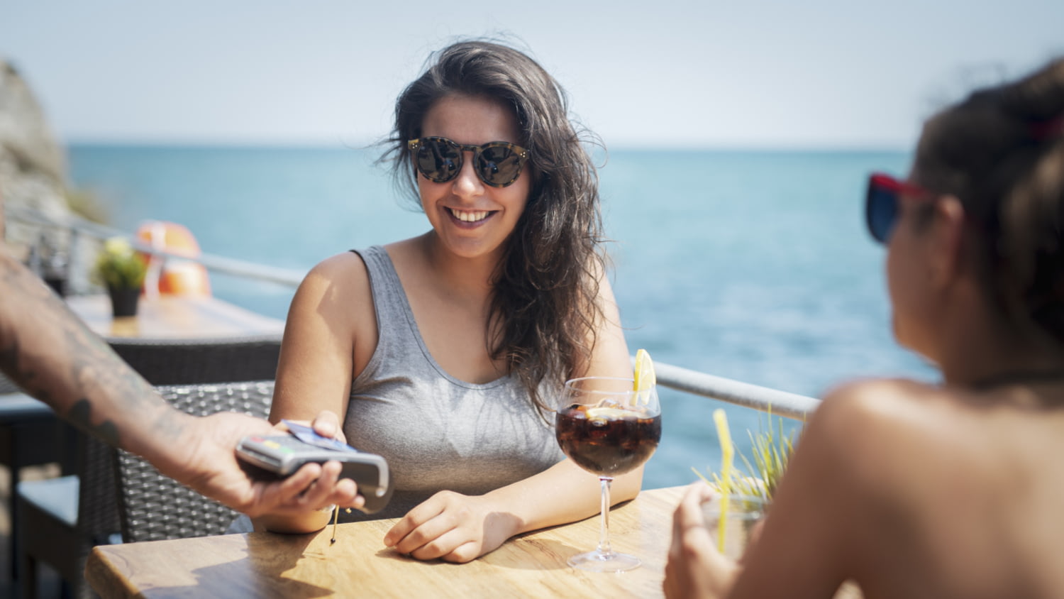 Junge Frau zahlt per Karte einen Cocktail in einer Strandbar