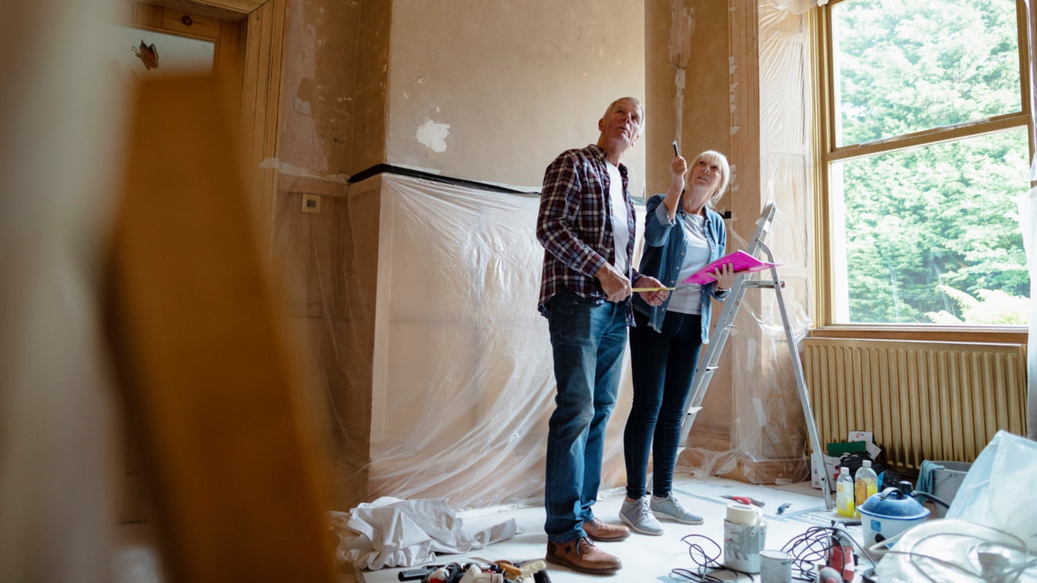 Pärchen steht in einer leeren Wohnung zwischen Utensilien zum Renovieren