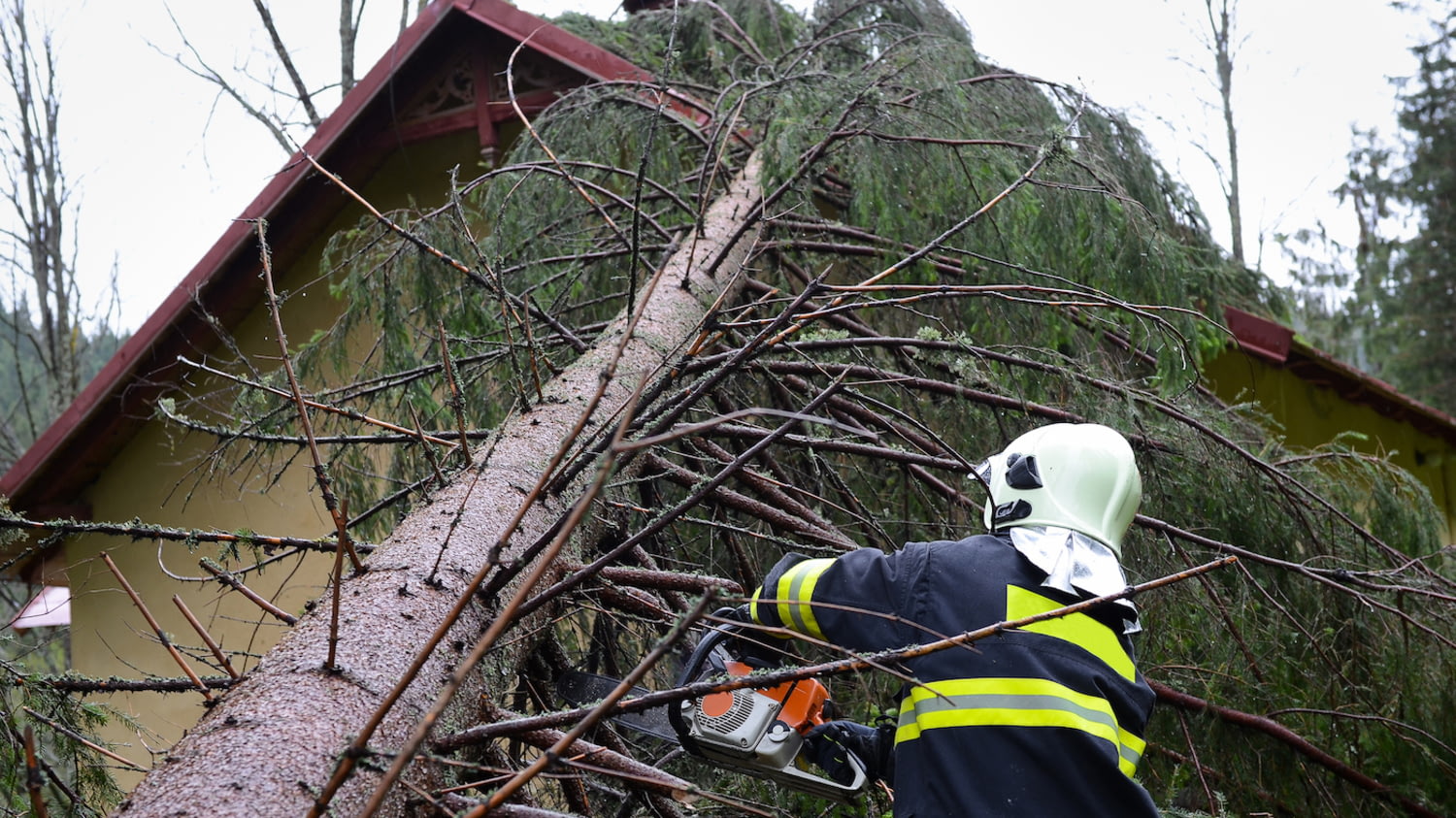 Ein Feuerwehrmann entfernt mit einer Kettensäge einen Baum, der auf ein Haus gestürzt ist.