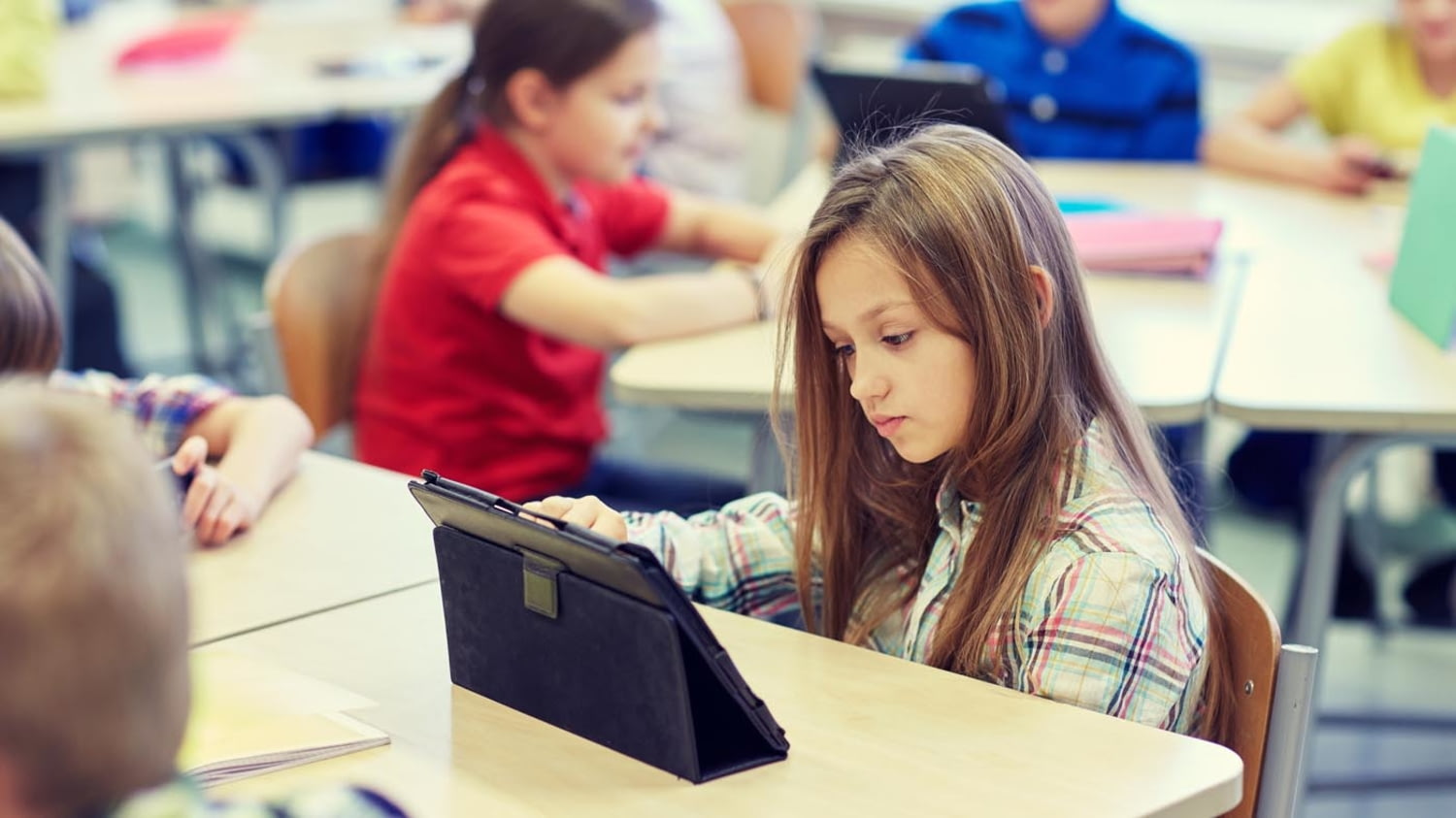 Eine Schülerin sitzt in einem Klassenzimmer und tippt auf den Bildschirm eines Tablet-PCs