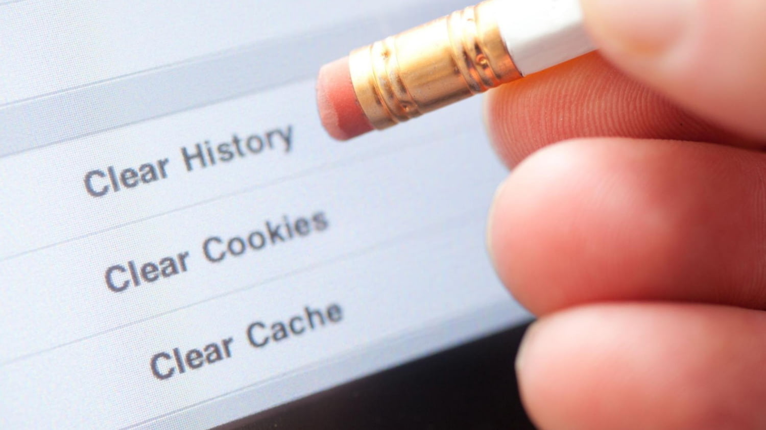 Jemand hält einen Bleistift mit Radiergummi vor einen PC-Bildschirm, um symbolisch Cookies zu löschen