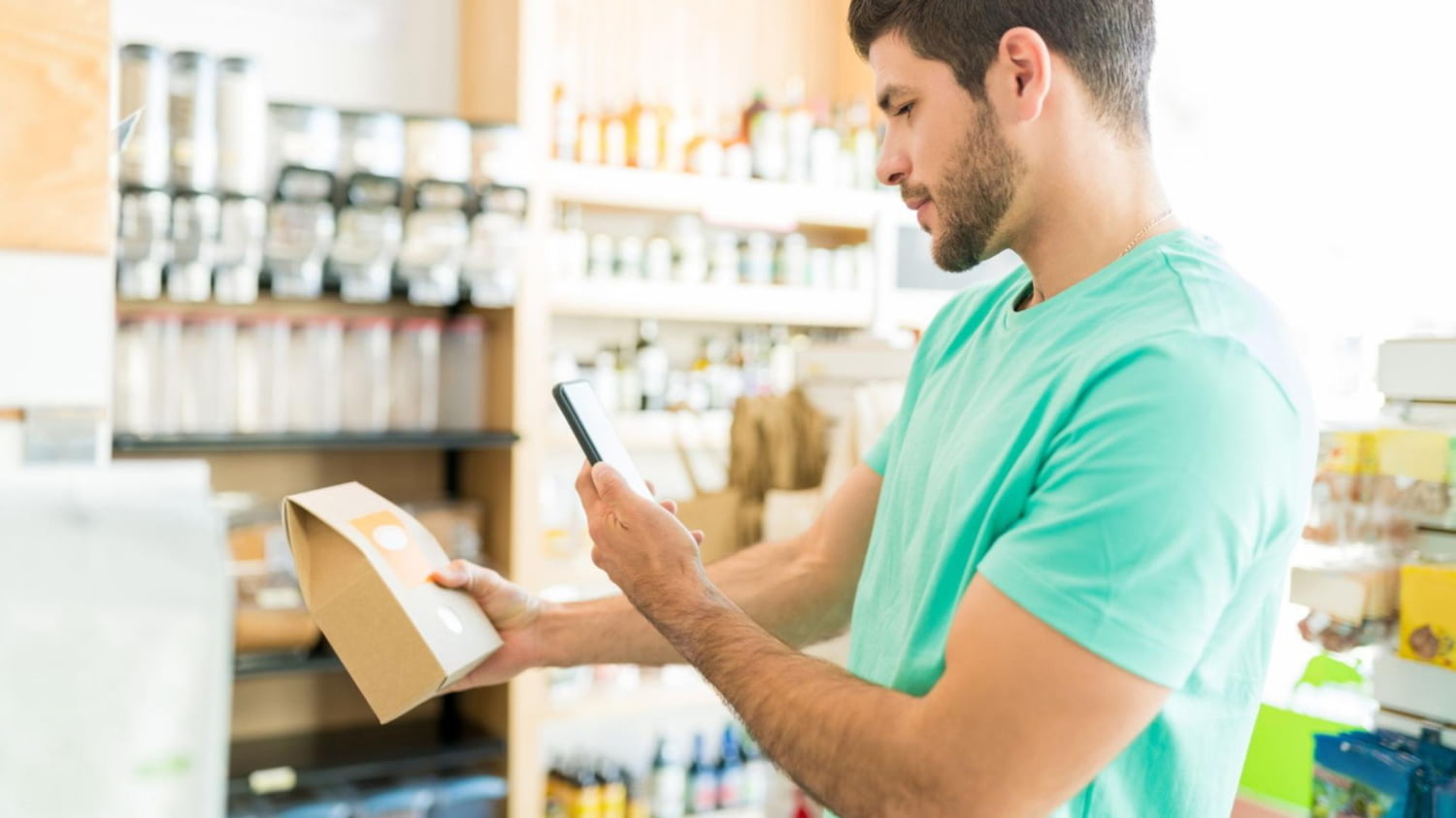 Eine Mann steht im Supermarkt und blickt auf das Display seines Smartphones