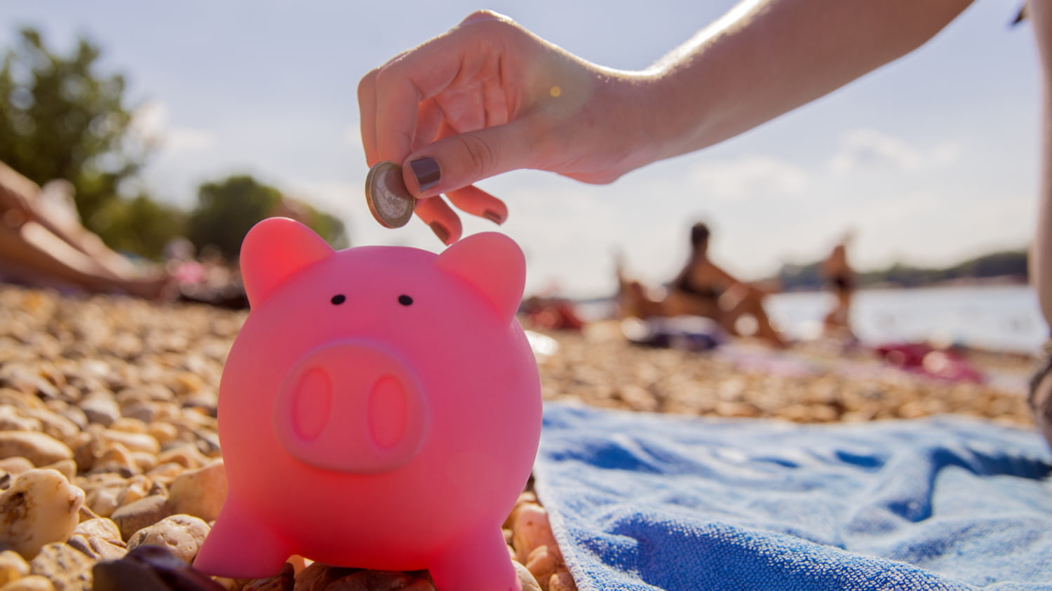 Frau am Strand steckt einen Euro in ein rosafarbenes Sparschwein