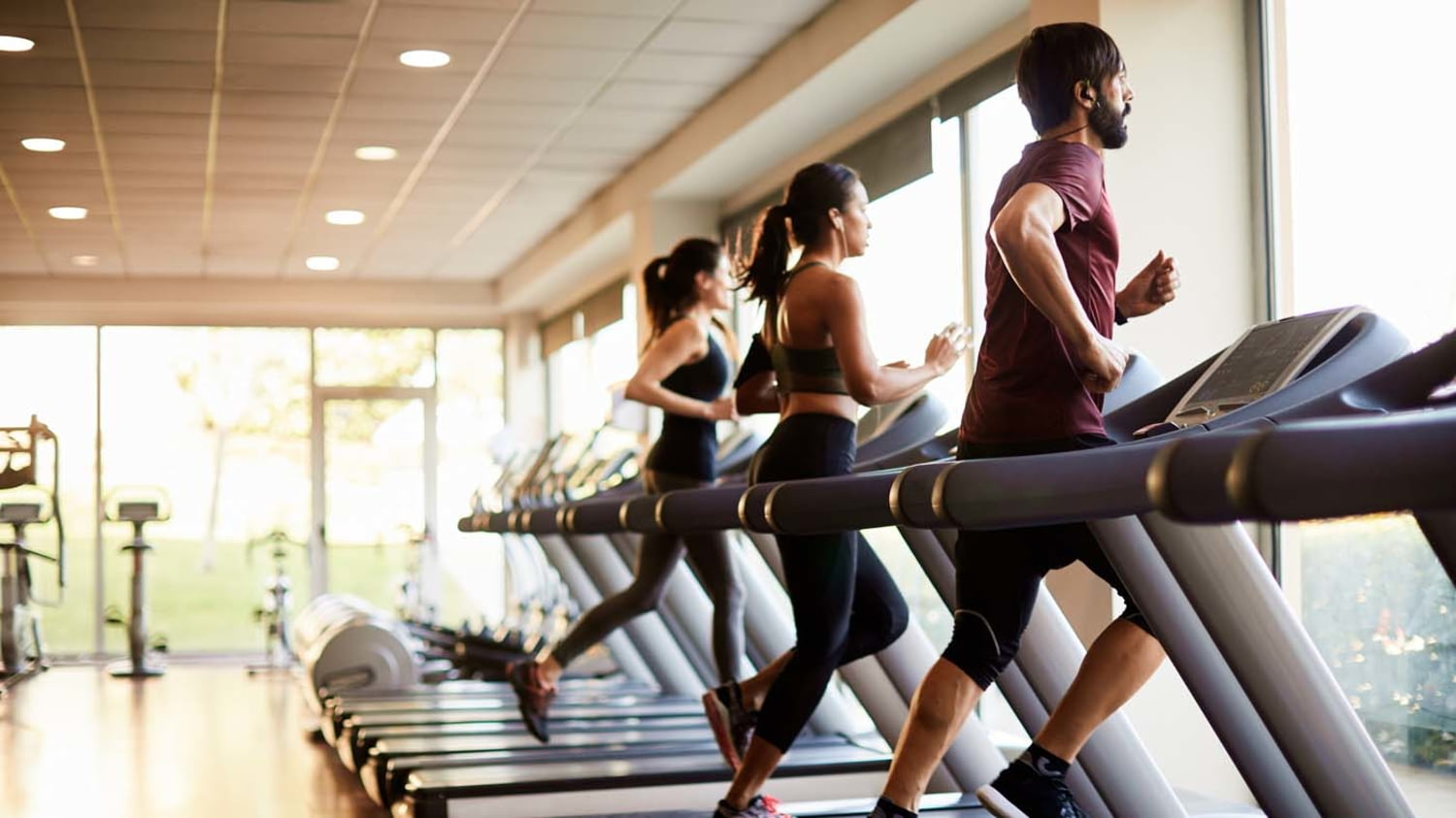 Ein Mann und zwei Frauen trainieren auf Laufbändern in einem Fitnessstudio