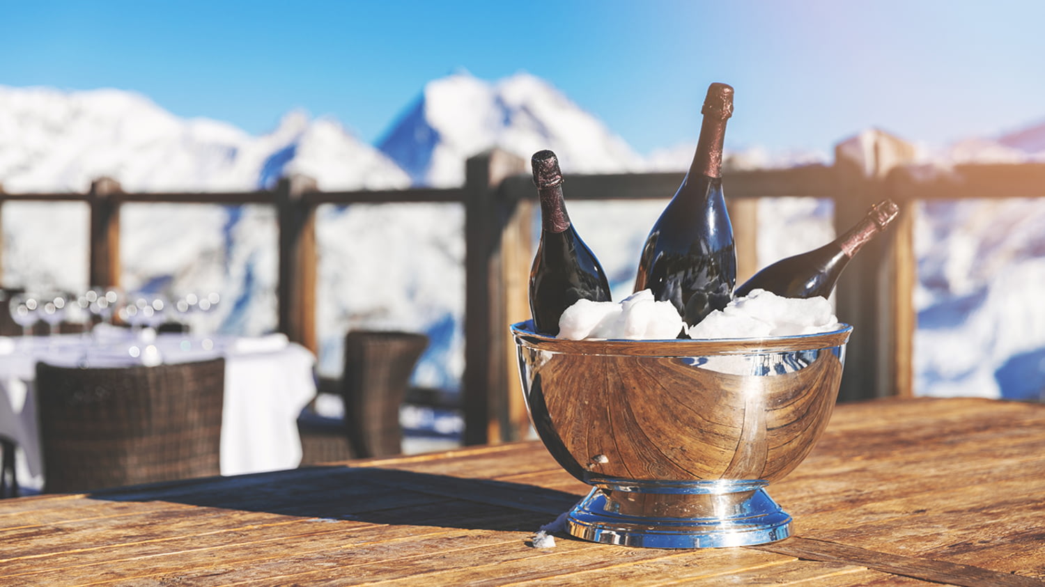 Drei Champagner-Flaschen im Kühler, die auf einem Tisch vor einem winterlichen Bergpanorama steht