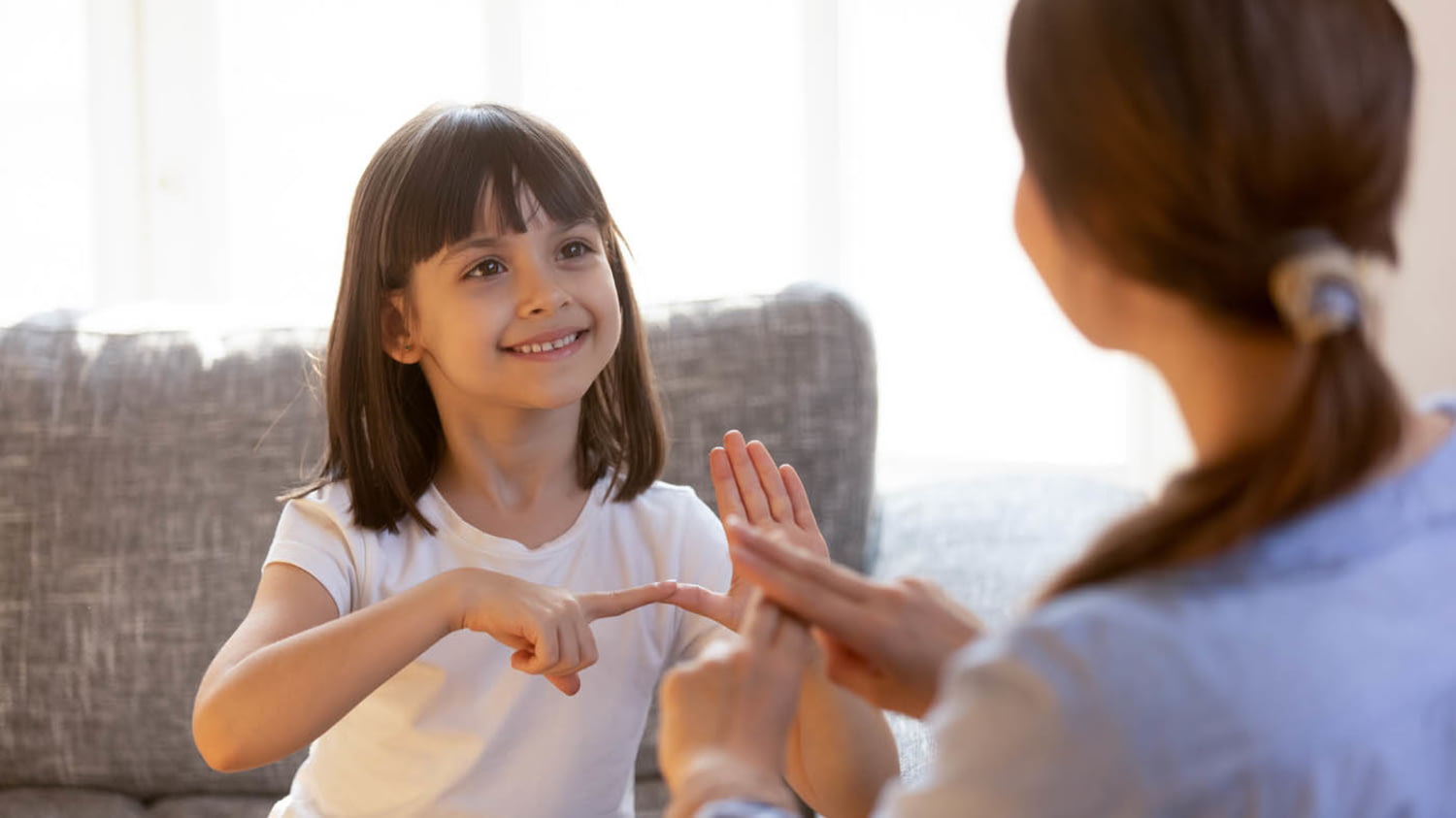 Ein Kind sitzt lächelnd auf einem Sofa und spielt mit einer Babysitterin