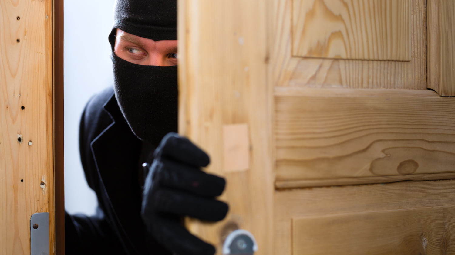 Ein Einbrecher schaut durch einen Türspalt eine Wohnung