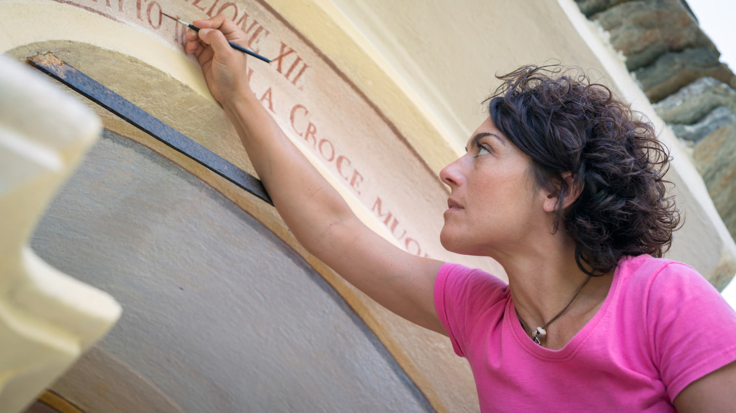 Eine Frau malt mit einem Pinsel die Inschrift an einem Kirchenportal nach