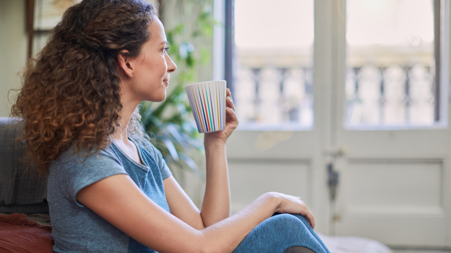 Eine junge Frau sitzt entspannt mit einem Becher Kaffee auf ihrem Sofa