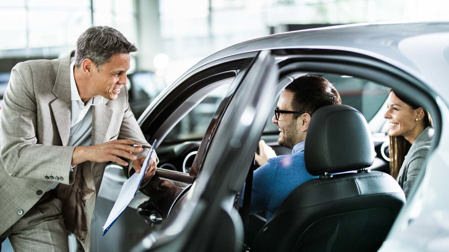 Autoverkäufer im Gespräch mit jungem Paar im Neuwagen