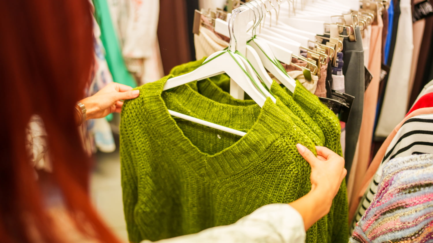 Eine Frau sieht sich in einem Textilgeschäft einen Pullover auf einem Kleiderständer an