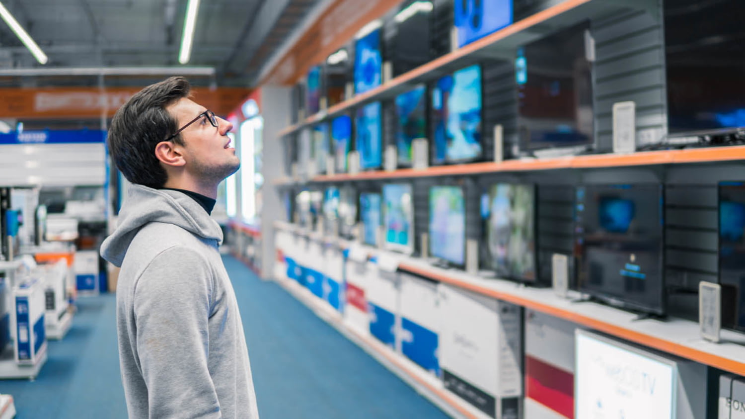 Ein junger Mann sieht sich in einem Elektrofachgeschäft das Angebot an Fernsehern an