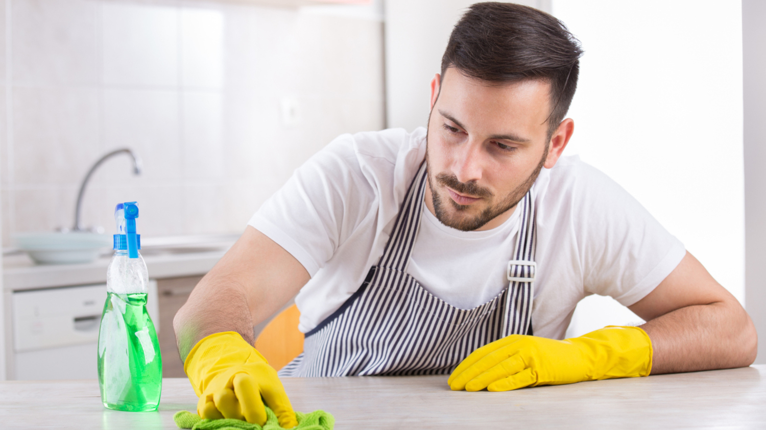 Junger Mann mit Schürze wischt einen Küchentisch