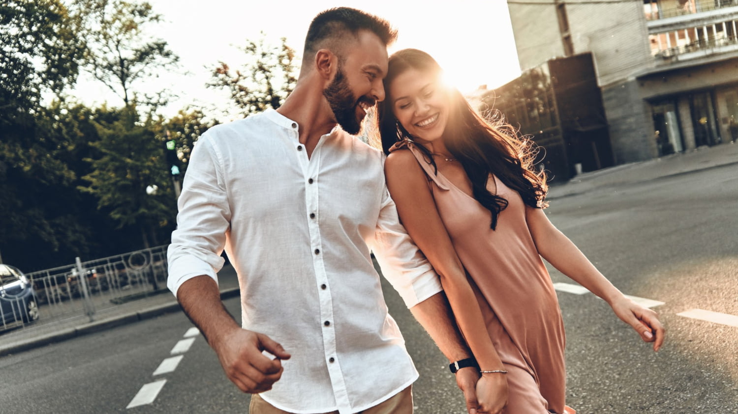 Ein junges Paar überquert lächelnd und händchenhaltend eine Straße