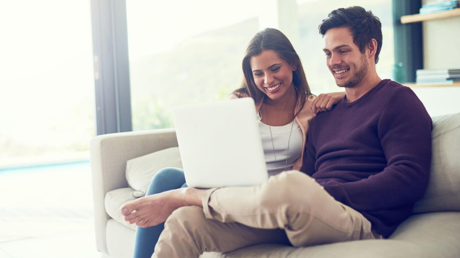 Ein glückliches Pärchen sitzt gemütlich mit dem Laptop auf dem Sofa