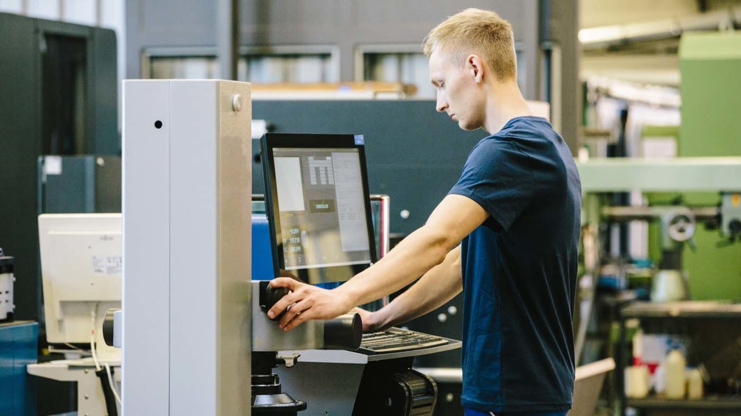 Ein junger Mann steht in einem Betrieb und steuert seine Arbeit an einer CNC-Maschine