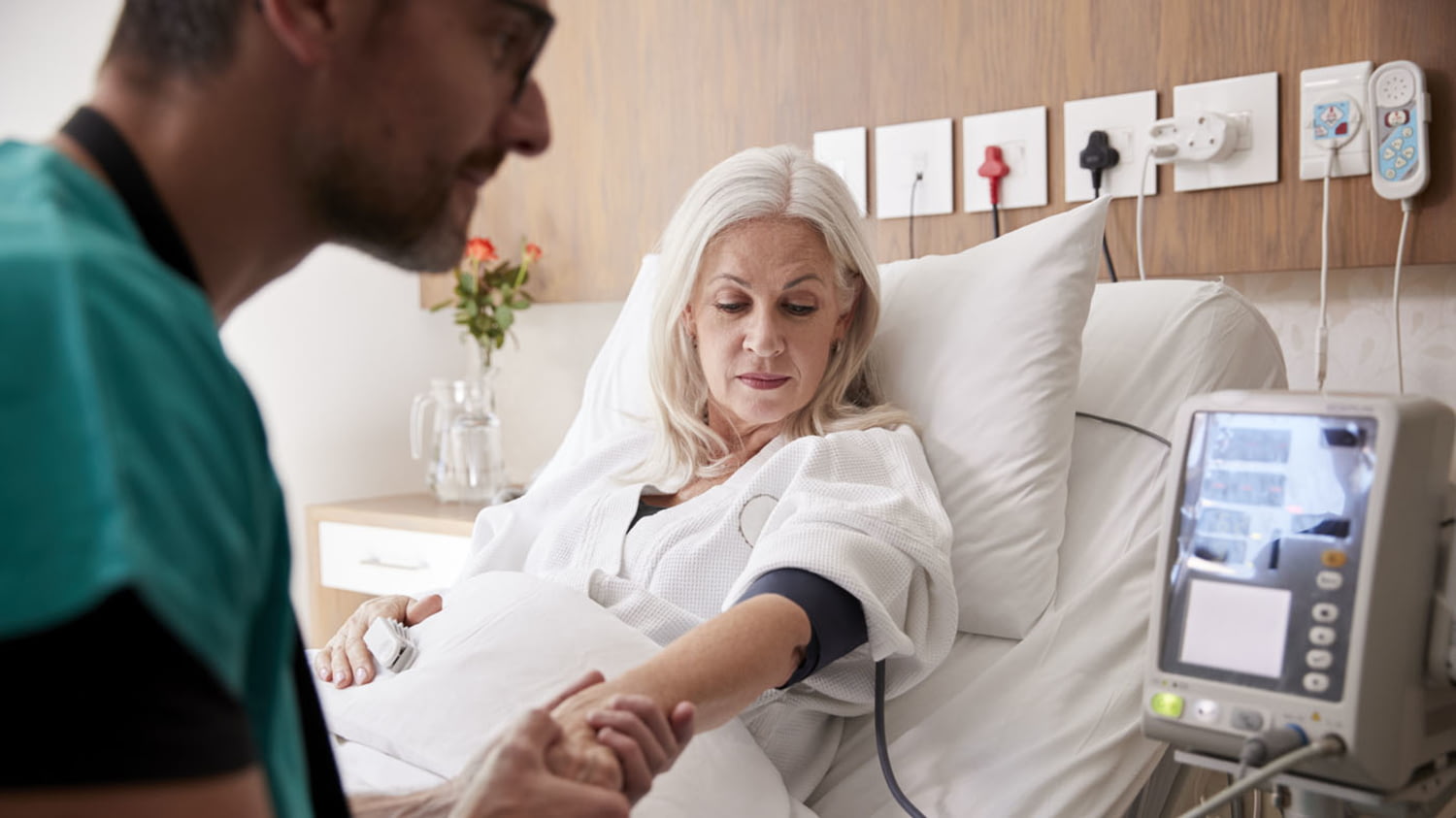 Ein Krankenpfleger misst den Blutdruck einer reiferen Patientin im Krankenhausbett