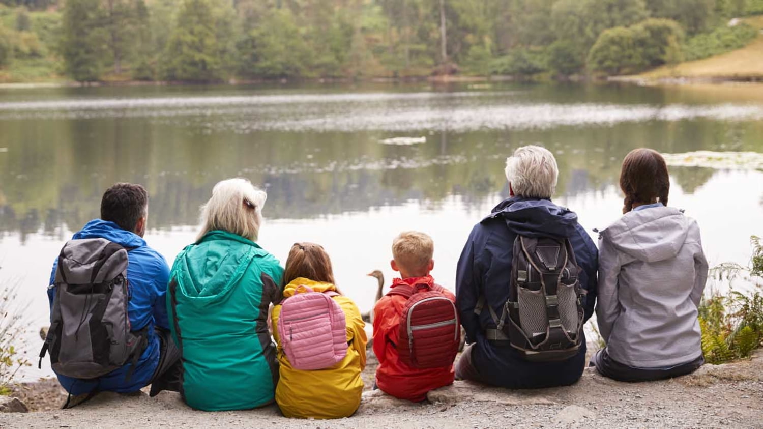 Drei Generationen einer Familie rasten bei einer Wanderung mit Blick auf einen See