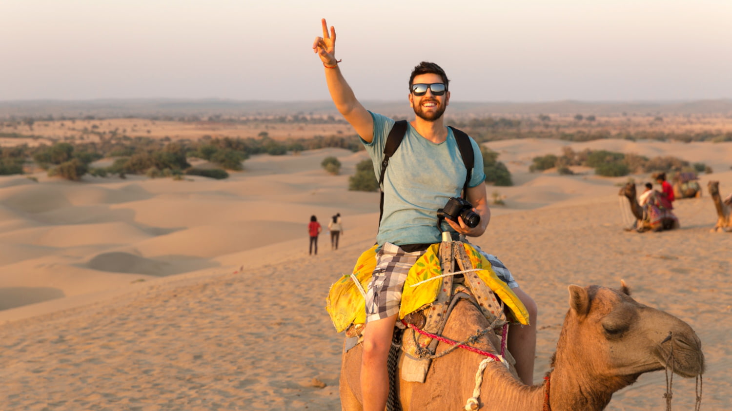 Ein Tourist sitzt auf einem Kamel, im Hintergrund Wüstenlandschaft