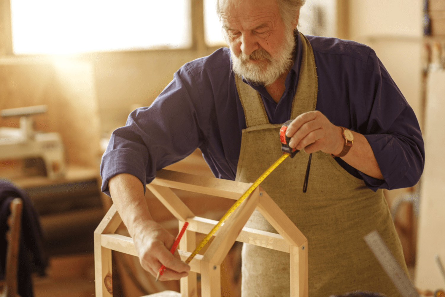 Ein älterer Mann baut und vermisst das Holzmodell eines Hauses