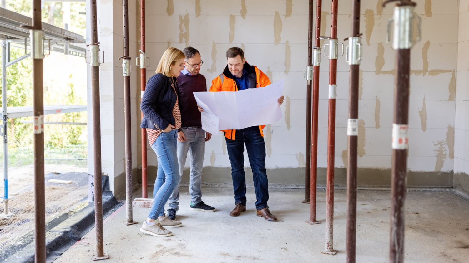 Junges Paar steht mit dem Bauleiter im Rohbau ihres neuen Hauses