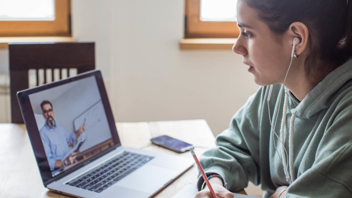 Eine junge Frau sitzt mit Kopfhörern an ihrem Schreibtisch und verfolgt an ihrem Laptop ein Online-Seminar
