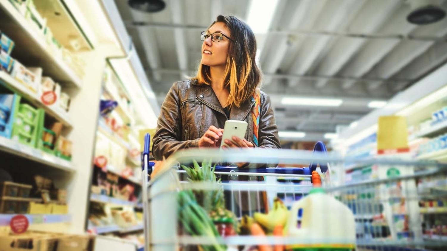 Junge Frau mit Einkaufswagen beim Lebensmitteleinkauf im Supermarkt