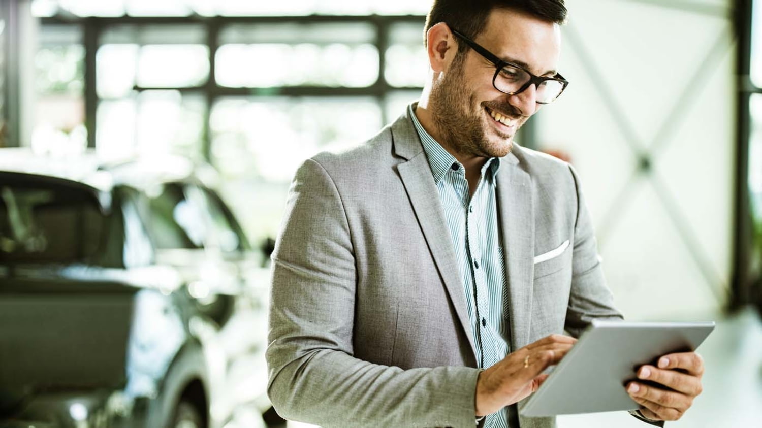 Ein gut gelaunter Verkäufer mit einem Tablet im Auto-Showroom
